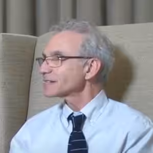 Man in glasses sitting indoors, wearing a tie.