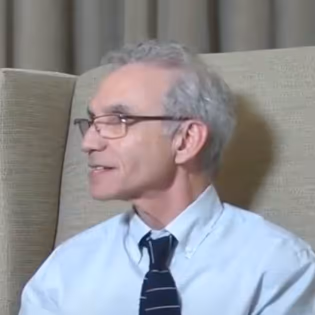 Man in glasses sitting indoors, wearing a tie.